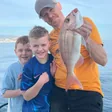 Father and sons posing with a sea bream caught on a family fishing trip in Málaga