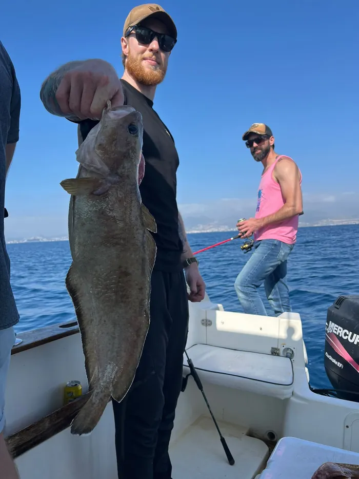 Angler showing a big catch while his friend keeps fishing in Málaga