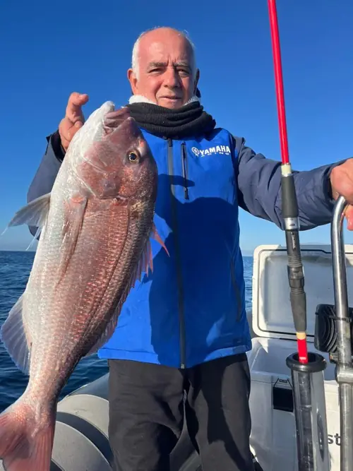 Angler in a blue jacket holding a fish caught next to a bent rod during a fishing trip in Málaga