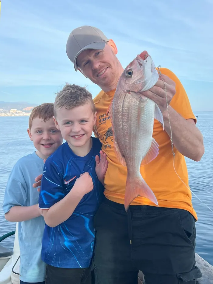 Father and sons posing with a sea bream caught on a family fishing trip in Málaga
