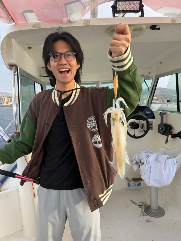 Smiling young man holding up a freshly caught squid on board during a squid fishing trip in Málaga