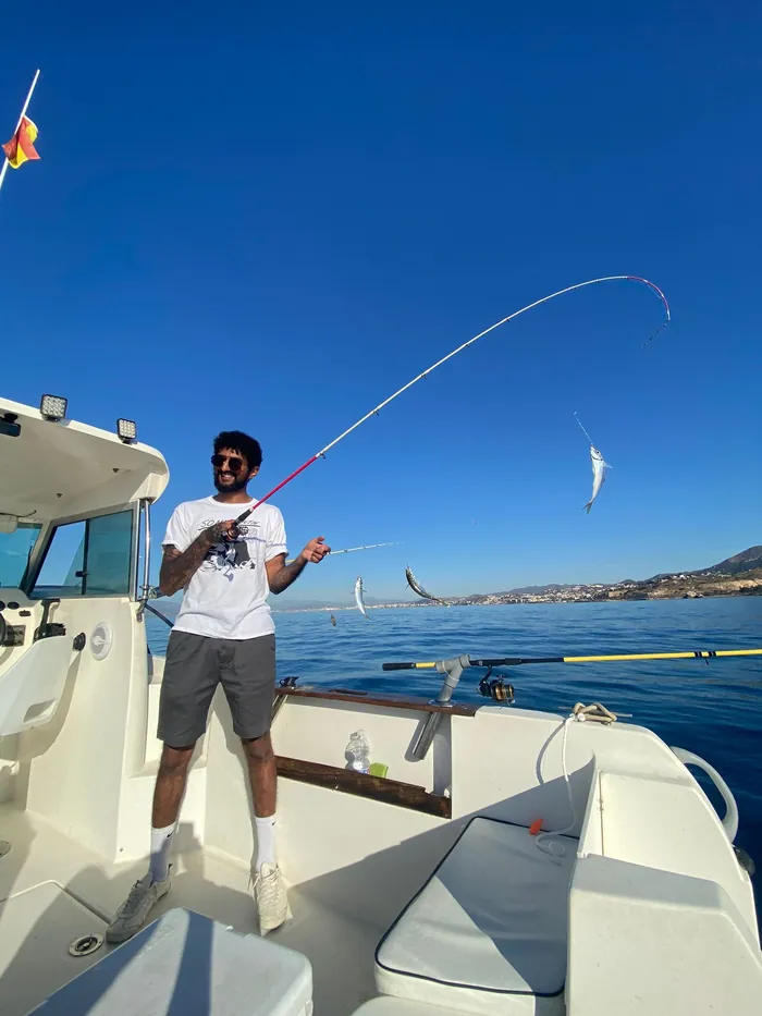 Angler reeling in a catch with a bent rod on board the fishing boat in Málaga